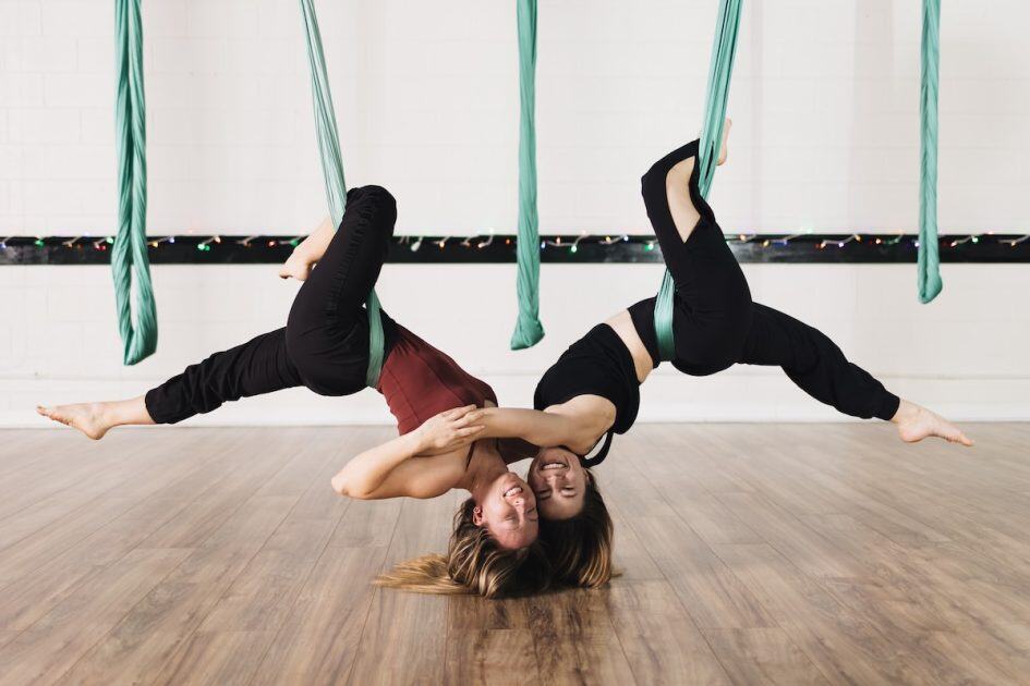 AIR Aerial Fitness - 2 female aerialists hang upside from silks in the peigon pose