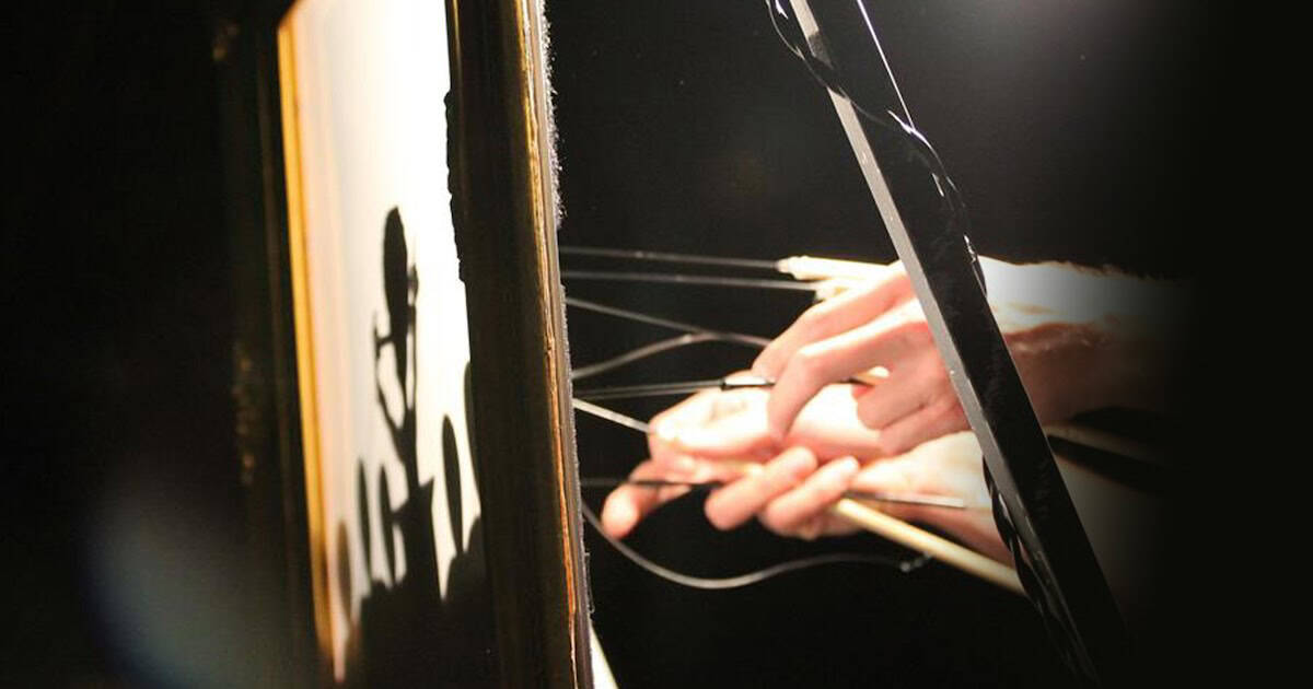 Hands holding metal sticks that operate shadow puppets behind a backlit screen
