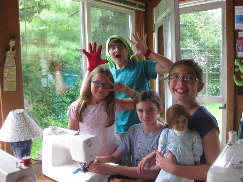 All Sewn Up Summer Camp - Campers gather around a sewing machine in front of windows.