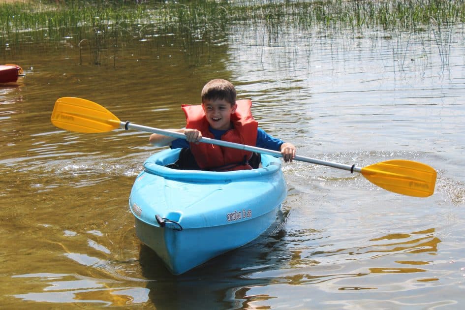 Child Kayaks on a lake with shallows plants behind
