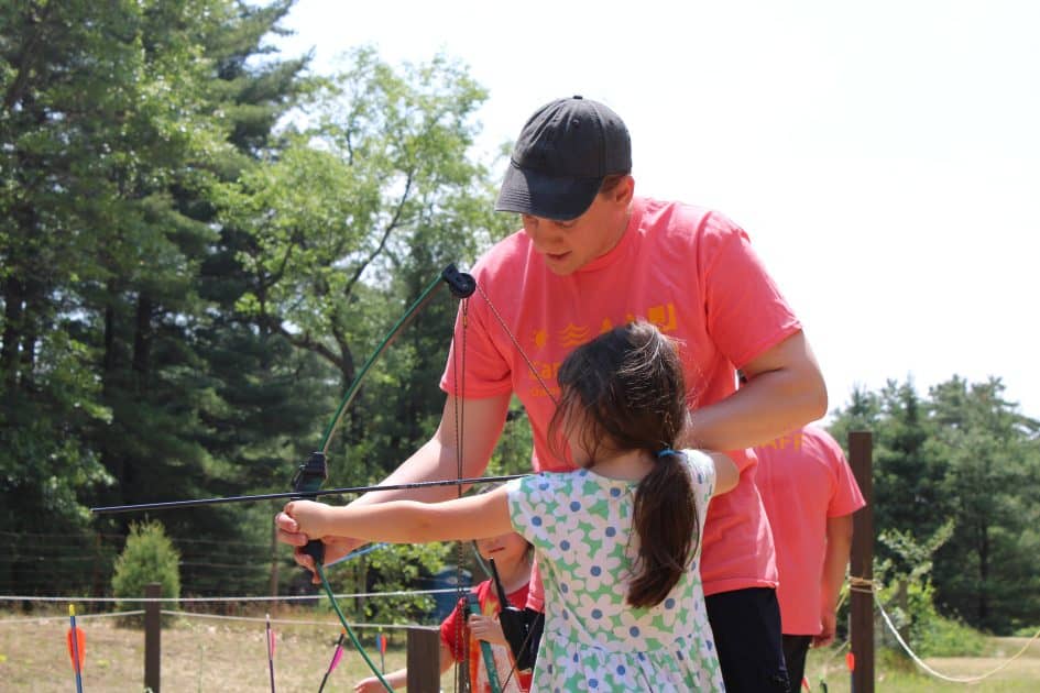 Camp Counselor helps a child shoot a bow