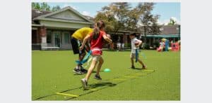 Kidokinetics - A girl playing flag football runs a drill through a rope ladder on the ground. A boy runs around a cone in the background