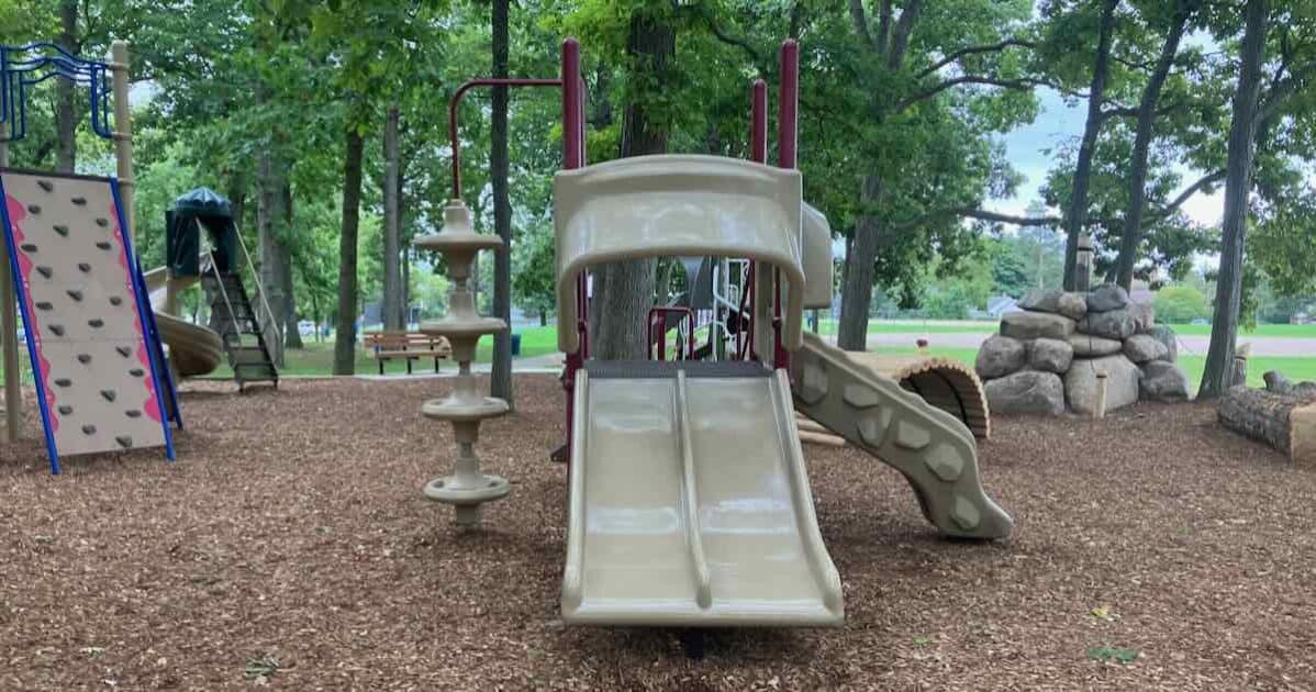 Allmendinger Park mini structure with 2 short racer slides, disc climber, and a rocky slide. Stairs (not visible in the photo) are also available. To the left are a climbing rock wall and stand alone twisty slide. To the right is the new rock tower and log tunnel