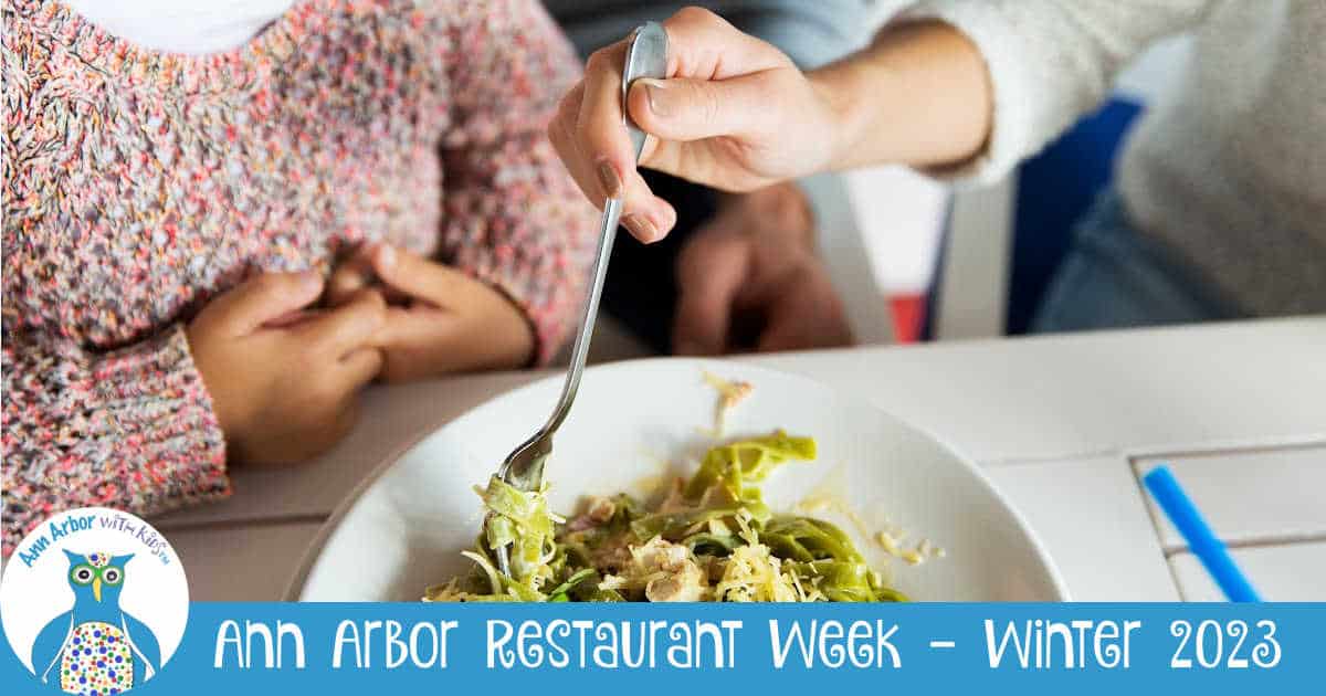 Ann Arbor Restaurant Week Winter 2023 - Parent's hand grabbing forkful of pesto pasta in front of child in pink sweater