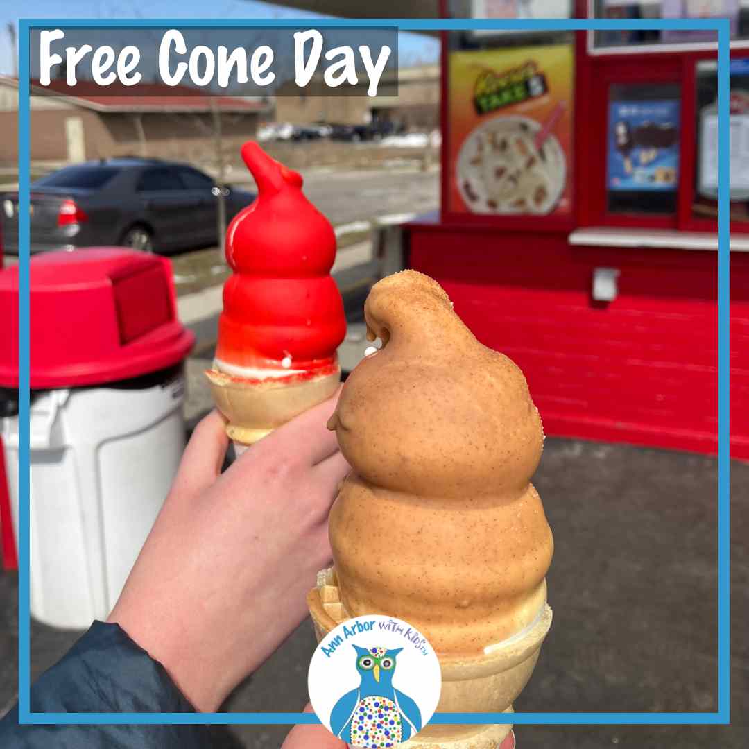 Free Cone Day - hands holding Dairy Queen cones - one dipped in cherry one in caramel - in front of the Ann Arbor Stadium Blvd Dairy Queen. Trash can & building with red bricks and large blizzard ads in the window is shown