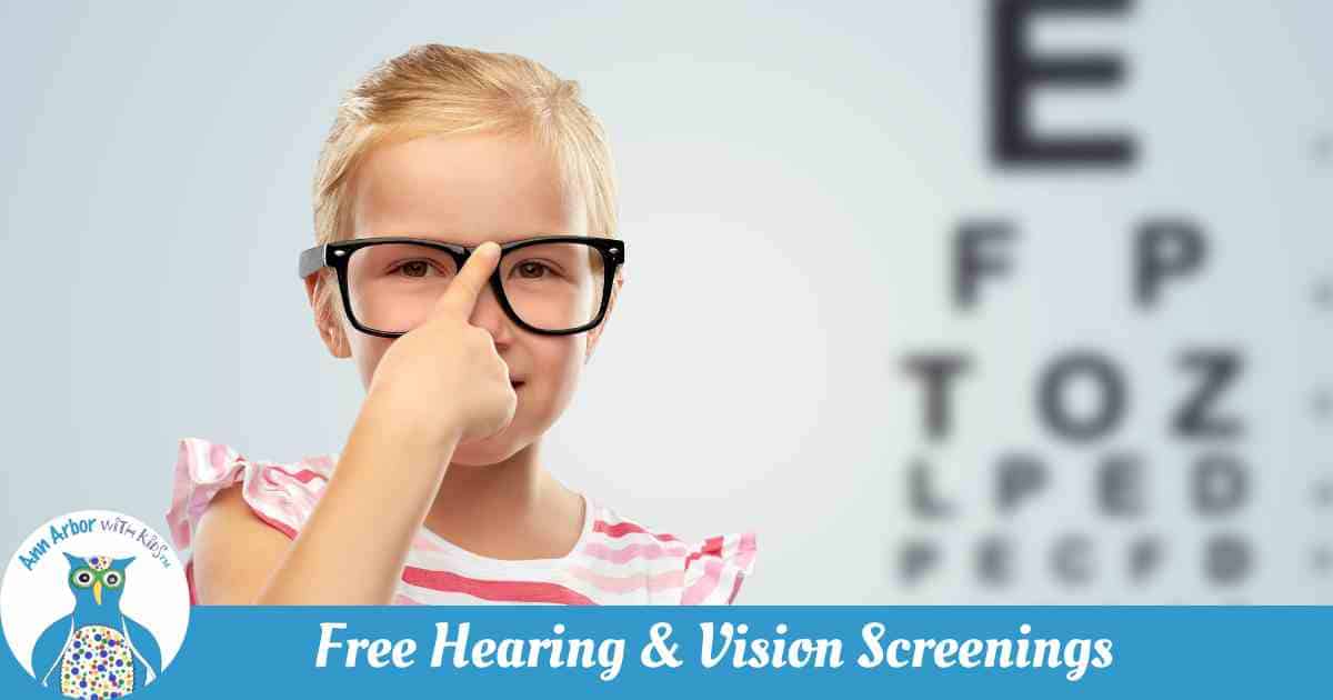 Free Hearing & Vision Screening - Girl pushes her glasses up with eye chart to her left.