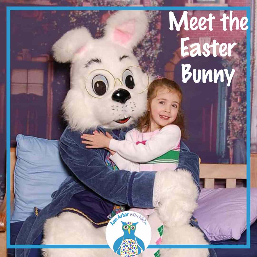 Meet the Easter Bunny - a girl in a striped sweater dress sits on Easter Bunny's lap on a bench in front of a brownstone background- Bunny is white with glasses and blue jacket.