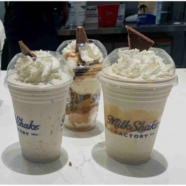 Milkshake Factory Shakes - Three milkshakes on store counter. The one in the back is a not shake - Peanut Butter Meltaway Cookie Sundae. Others are Gourmet Shakes Confetti Frosted Cupcake and Salted Caramel Pretzel