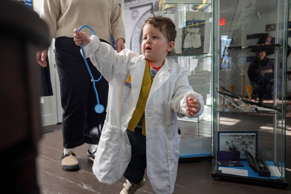 UM Med School History Exhibit - A toddler boy tries on a UM Medicine lab coat and stethoscope
