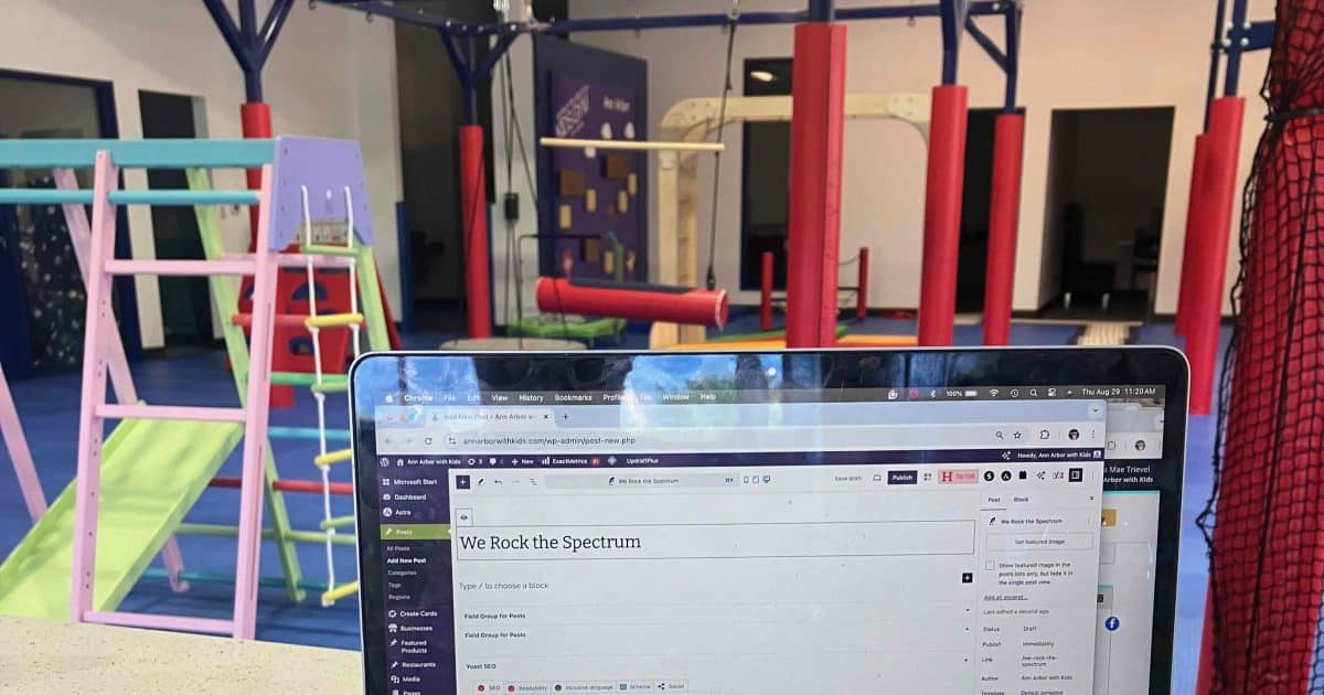 We Rock the Spectrum - laptop sitting on the lobby bar for parental seating with a view of gym equipment behind it including a slide and climber and sensory swings. The rock wall is in the distance
